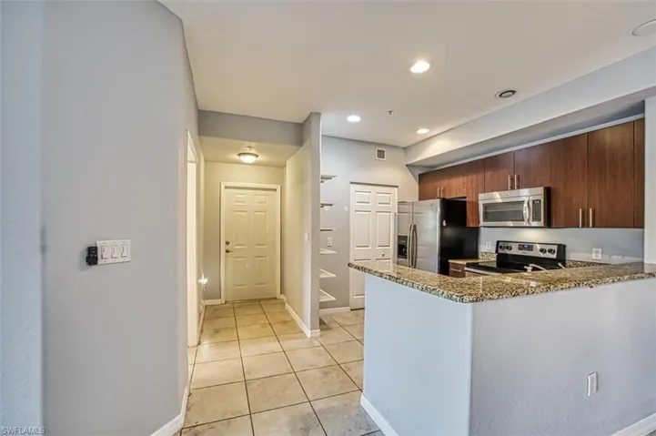 Kitchen featuring kitchen peninsula, appliances with stainless steel finishes, light tile patterned floors, and stone countertops