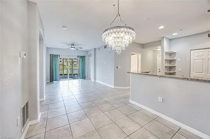 Tiled empty room with ceiling fan with notable chandelier