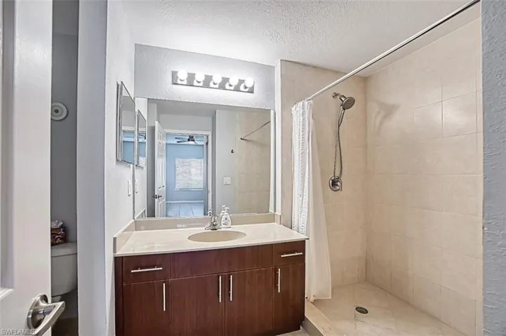 Bathroom featuring curtained shower, toilet, a textured ceiling, and vanity