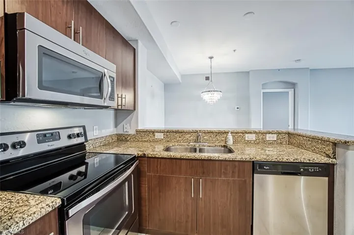 Kitchen with an inviting chandelier, light stone countertops, stainless steel appliances, sink, and kitchen peninsula