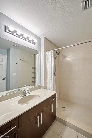 Bathroom with tile patterned flooring, walk in shower, a textured ceiling, and vanity