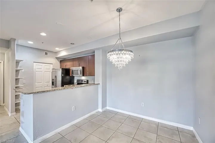 Kitchen with light tile patterned floors, kitchen peninsula, stainless steel appliances, and light stone countertops
