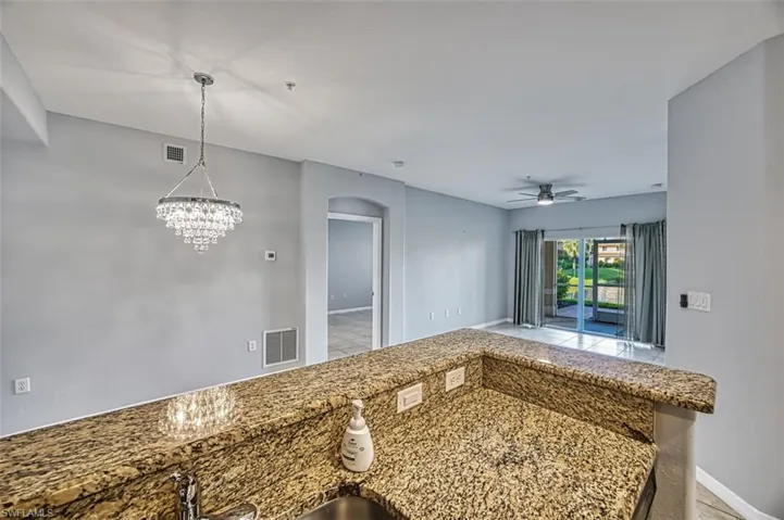 Kitchen featuring ceiling fan with notable chandelier, pendant lighting, light tile patterned floors, kitchen peninsula, and light stone counters