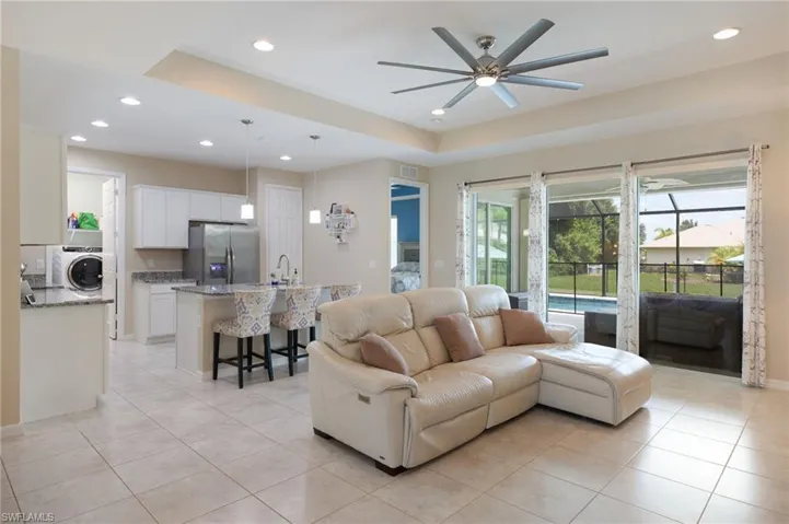 Living room with light tile patterned floors, ceiling fan, a tray ceiling, washer / dryer, and sink