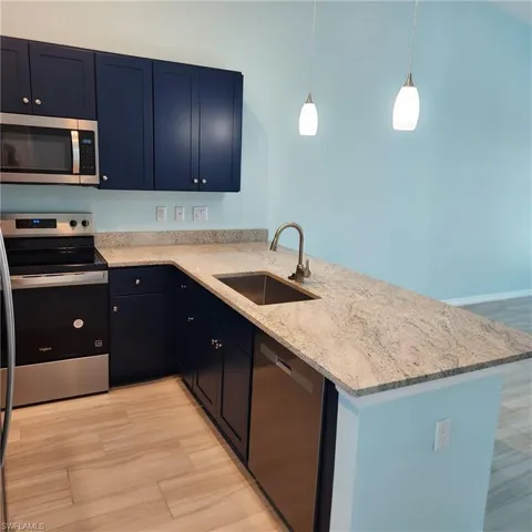 Kitchen featuring stainless steel appliances, a sink, a peninsula, light stone countertops, and light wood finished floors