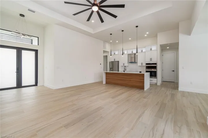 Kitchen featuring appliances with stainless steel finishes, white cabinets, pendant lighting, an island with sink, and a tray ceiling
