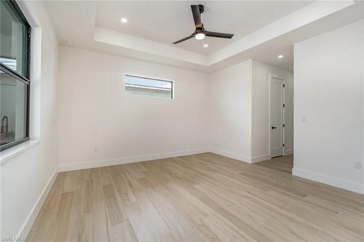 Spare room with light hardwood / wood-style floors, ceiling fan, and a tray ceiling
