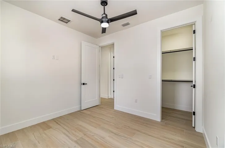Unfurnished bedroom featuring a spacious closet, light hardwood / wood-style floors, a closet, and ceiling fan