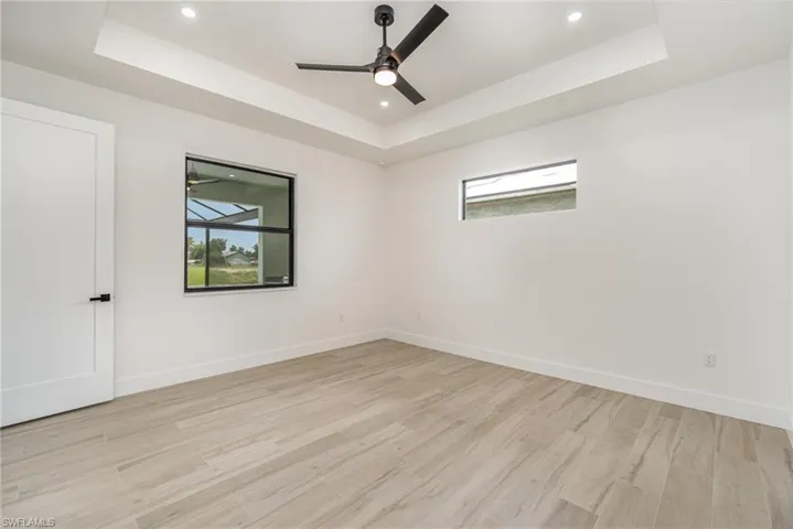 Unfurnished room with light hardwood / wood-style floors, ceiling fan, and a raised ceiling