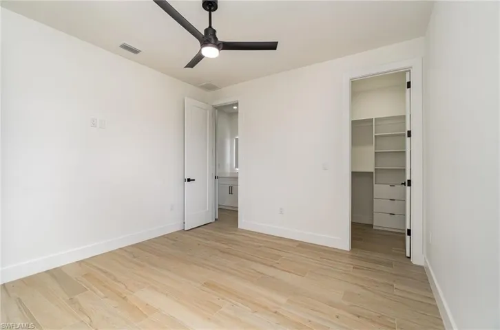 Unfurnished bedroom featuring a closet, light hardwood / wood-style flooring, a spacious closet, and ceiling fan