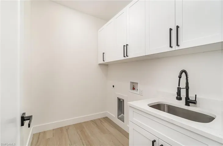 Clothes washing area featuring light wood-type flooring, hookup for a washing machine, cabinets, electric dryer hookup, and sink