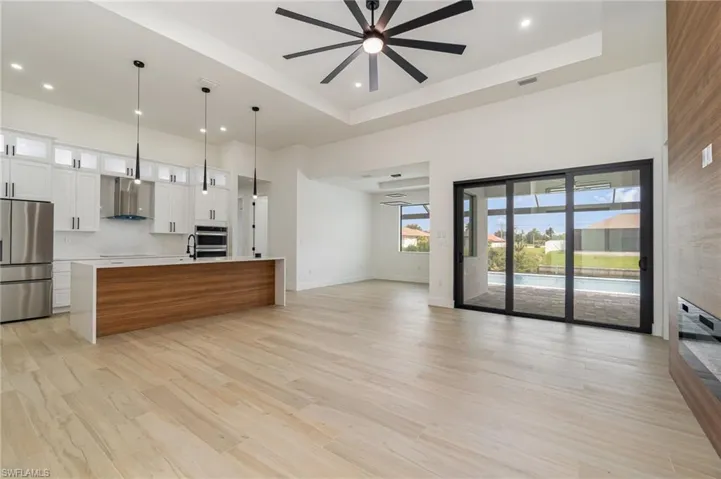 Kitchen featuring appliances with stainless steel finishes, a center island with sink, wall chimney range hood, pendant lighting, and ceiling fan