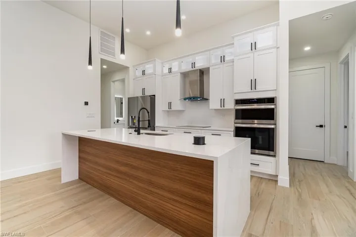 Kitchen with wall chimney range hood, light hardwood / wood-style flooring, stainless steel appliances, and an island with sink