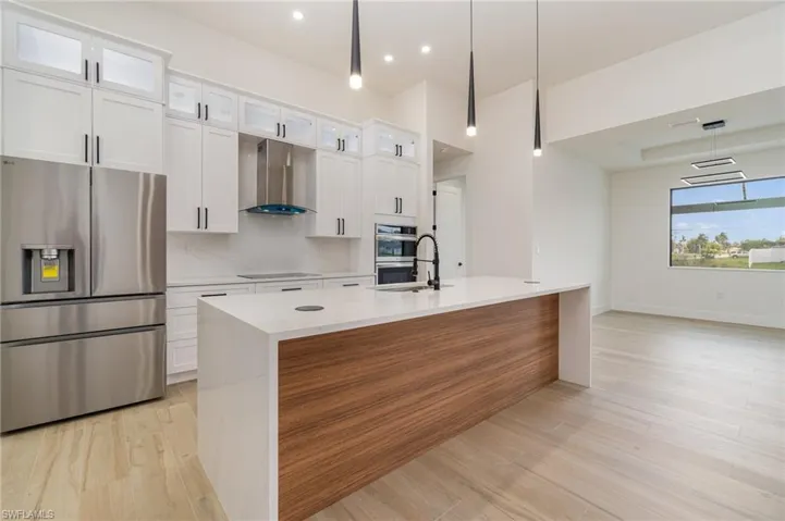 Kitchen with light hardwood / wood-style flooring, stainless steel appliances, white cabinets, hanging light fixtures, and wall chimney exhaust hood