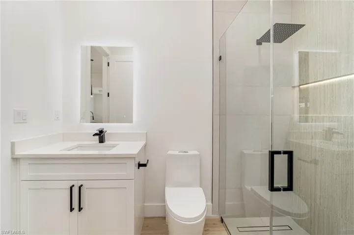 Bathroom with hardwood / wood-style flooring, a shower with door, toilet, and vanity