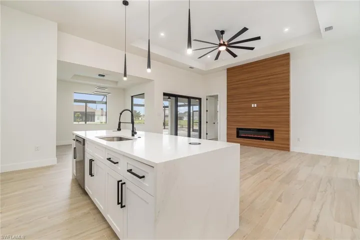 Kitchen featuring white cabinets, a kitchen island with sink, a raised ceiling, sink, and a large fireplace
