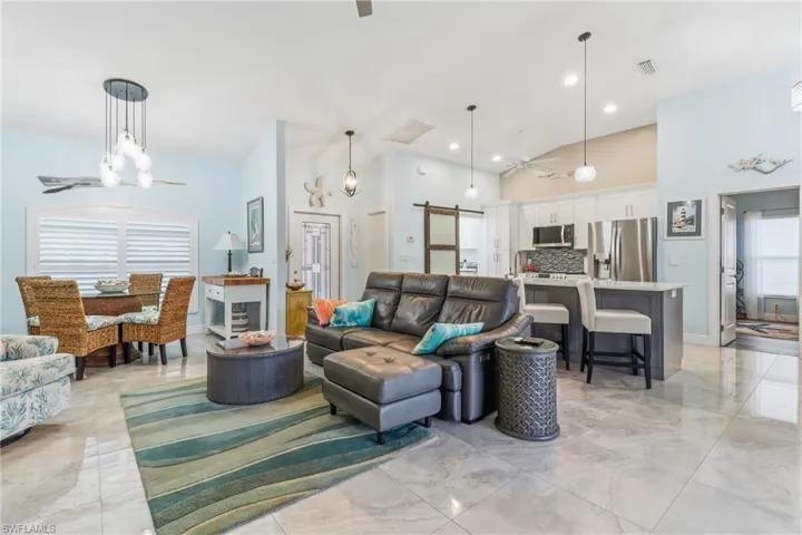 Living area with ceiling fan, a barn door, light marble finish floors, high vaulted ceiling, and a chandelier
