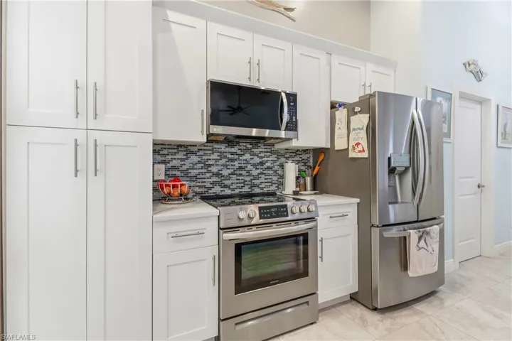 Kitchen featuring appliances with stainless steel finishes, white cabinets, tasteful backsplash, and light stone counters
