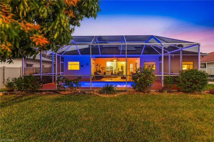 Back of property at dusk with a lanai, a sunroom, a lawn, and an outdoor pool