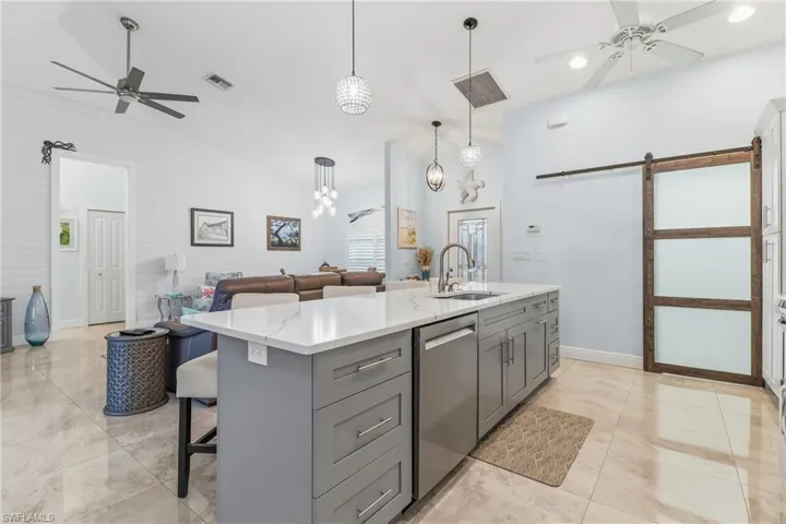 Kitchen with a ceiling fan, a barn door, gray cabinets, a breakfast bar, and lofted ceiling