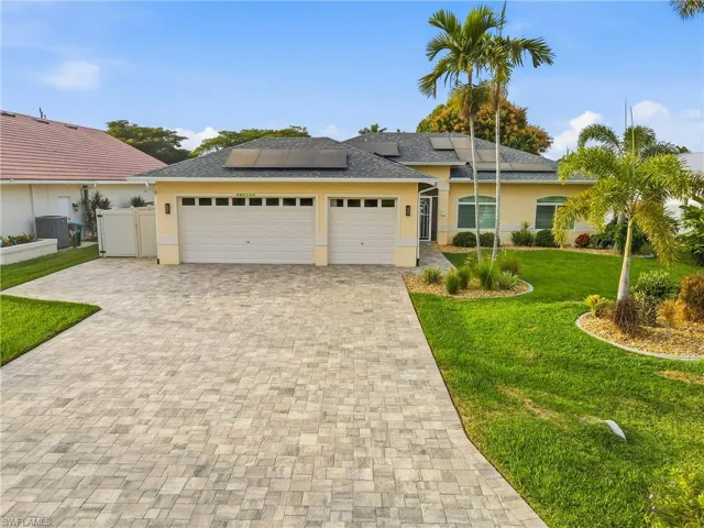Single story home featuring a front yard, decorative driveway, a garage, roof mounted solar panels