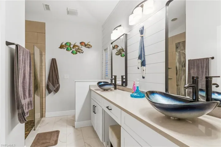 Bathroom featuring light marble finish flooring, double vanity, and a shower with shower door