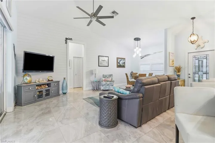 Living room featuring ceiling fan, light marble finish floors, lofted ceiling, a chandelier, and wood walls