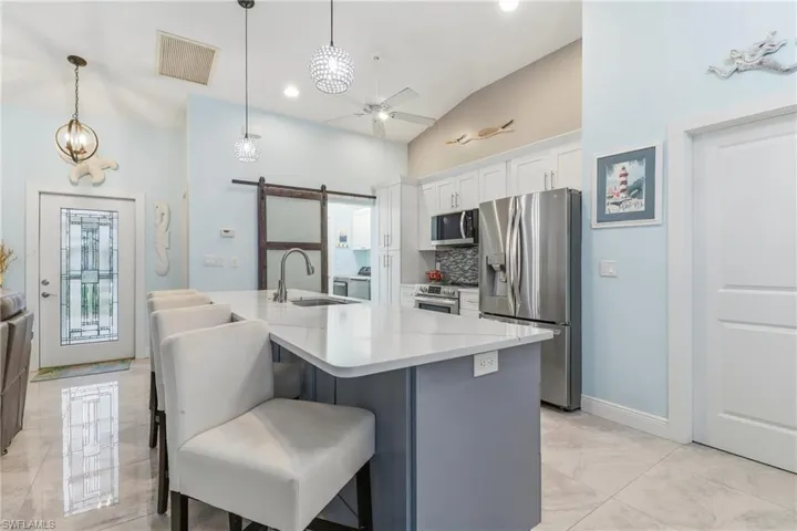 Kitchen featuring a barn door, stainless steel appliances, tasteful backsplash, a breakfast bar area, and an island with sink