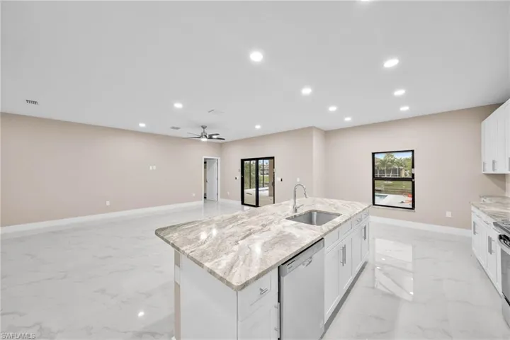 Kitchen featuring light stone counters, white cabinets, sink, a kitchen island with sink, and appliances with stainless steel finishes