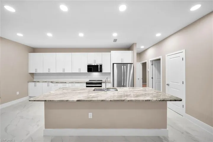 Kitchen with light stone counters, sink, a large island, white cabinetry, and appliances with stainless steel finishes