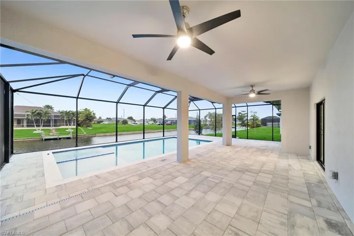 View of swimming pool with a water view, ceiling fan, a lawn, a lanai, and a patio area