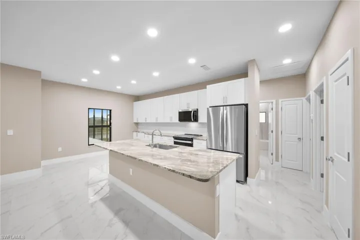 Kitchen with light stone counters, white cabinetry, appliances with stainless steel finishes, sink, and a kitchen island with sink