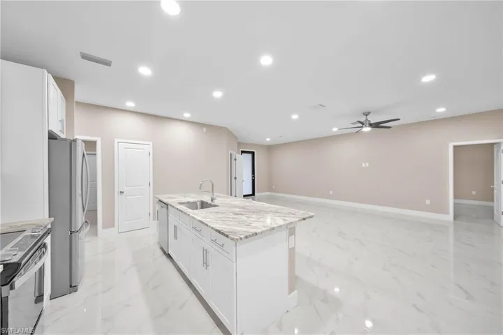 Kitchen with a center island with sink, white cabinetry, appliances with stainless steel finishes, light stone countertops, and sink
