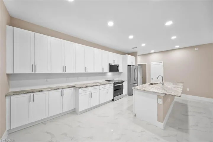 Kitchen with white cabinetry, stainless steel appliances, and an island with sink