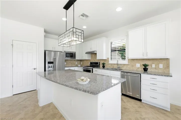 Kitchen featuring appliances with stainless steel finishes, white cabinets, light stone countertops, a center island, and recessed lighting