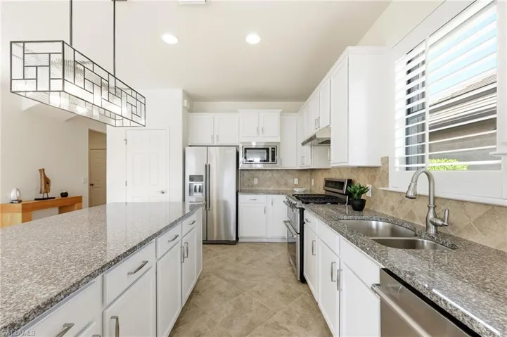Kitchen featuring stainless steel appliances, dark stone countertops, white cabinets, recessed lighting, and hanging light fixtures