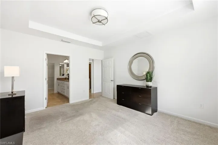Unfurnished bedroom with light carpet, connected bathroom, and a tray ceiling