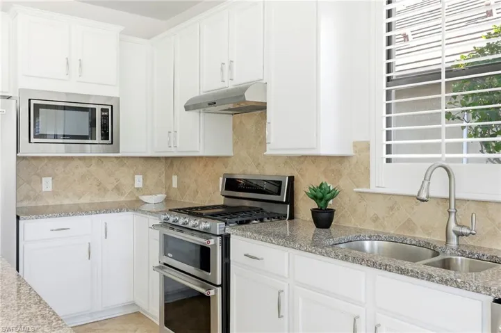 Kitchen with stainless steel appliances, white cabinetry, light stone countertops, and under cabinet range hood