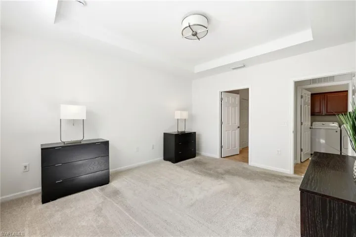 Unfurnished bedroom with washer / clothes dryer, light colored carpet, and a tray ceiling