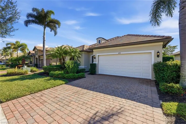 View of front facade featuring decorative driveway, stucco siding, a front lawn, and an attached garage