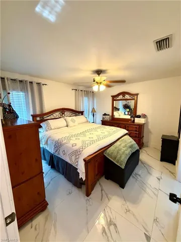 Bedroom with light marble finish floors, multiple windows, and ceiling fan