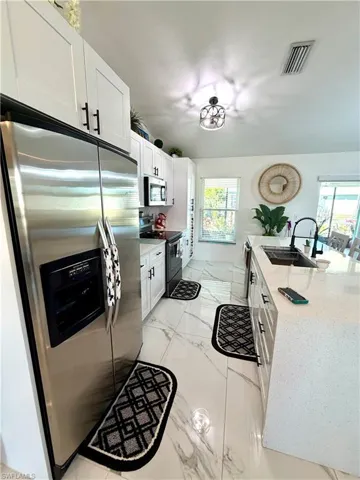 Kitchen with stainless steel appliances, white cabinets, light marble finish floors, light stone countertops, and a center island with sink