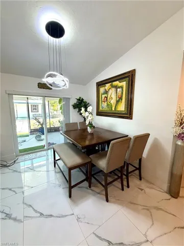 Dining room with light marble finish flooring, vaulted ceiling, and suspended lighting