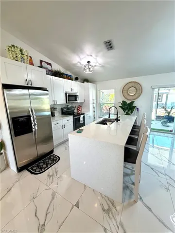 Kitchen featuring stainless steel appliances, light stone countertops, white cabinetry, light marble finish flooring, and a kitchen island with sink