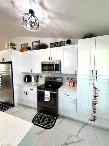 Kitchen with stainless steel appliances, white cabinets, light stone countertops, light marble finish floors, and backsplash