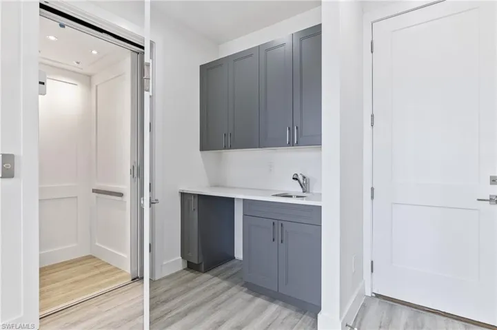 Bar with light wood-style flooring, elevator, gray cabinets, and light stone countertops