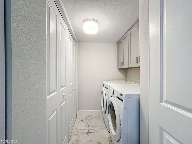 Laundry area featuring light marble finish flooring, a textured ceiling, washing machine and dryer, and cabinet space