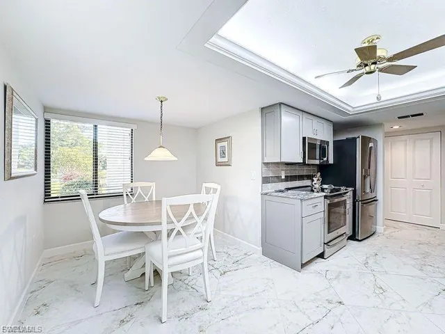 Kitchen with gray cabinetry, appliances with stainless steel finishes, light marble finish flooring, and decorative backsplash