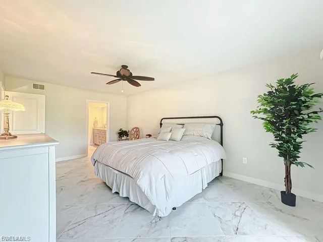 Bedroom featuring light marble finish floors, a ceiling fan, and ensuite bath