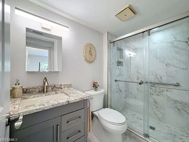 Bathroom with vanity, a marble finish shower, and a textured wall